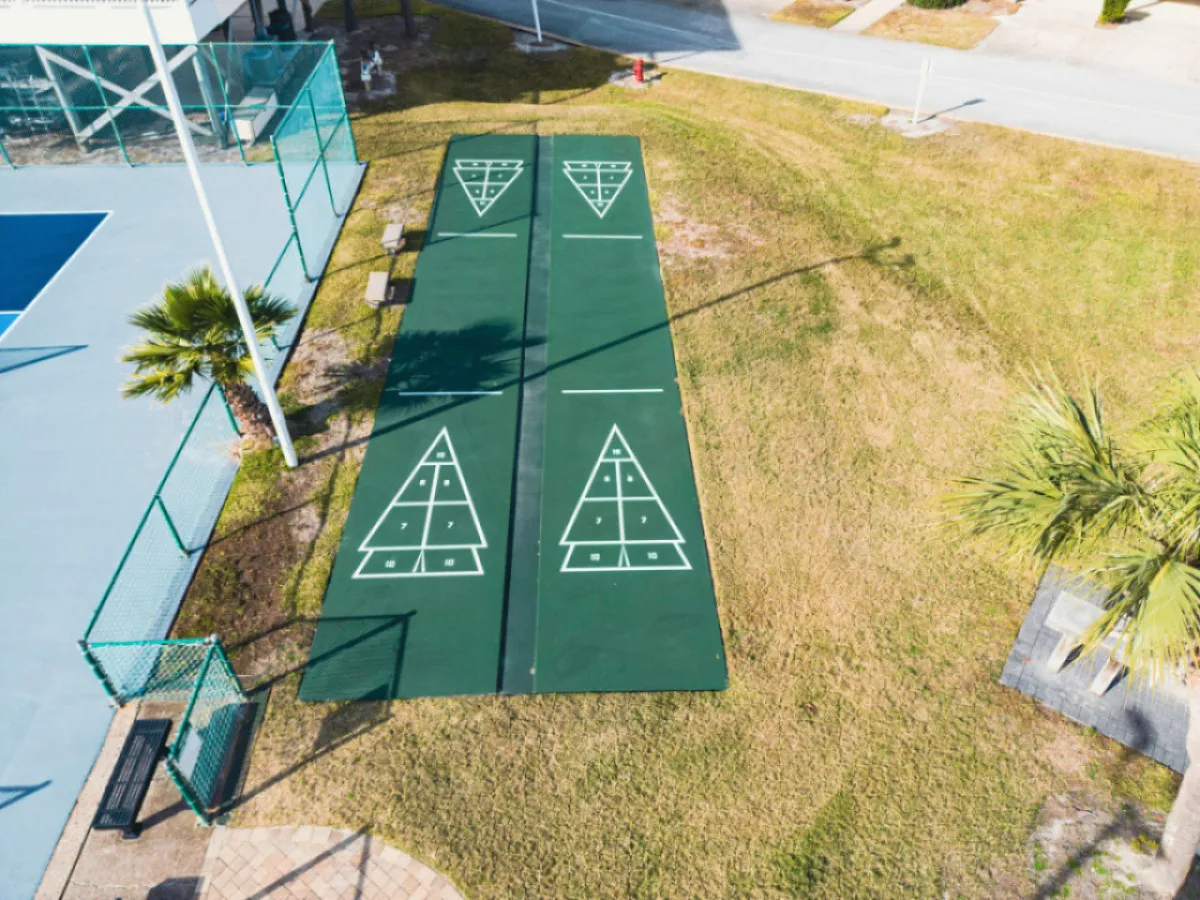 This scene shows the shuffleboard courts nestled among palm trees and grassy areas, with benches inviting players and onlookers to relax. The recreational space is designed for friendly competition and camaraderie, encapsulating the laid-back yet playful atmosphere of the resort.