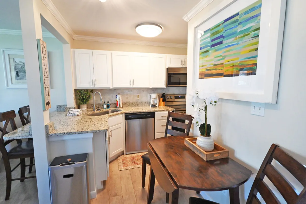 This image captures the heart of the kitchen and dining area, featuring granite countertops, stainless steel appliances, a small wooden dining table with chairs, and colorful abstract wall art. The scene is welcoming and relaxed, with hints of meal preparation, casual dining, and socializing in an intimate space.